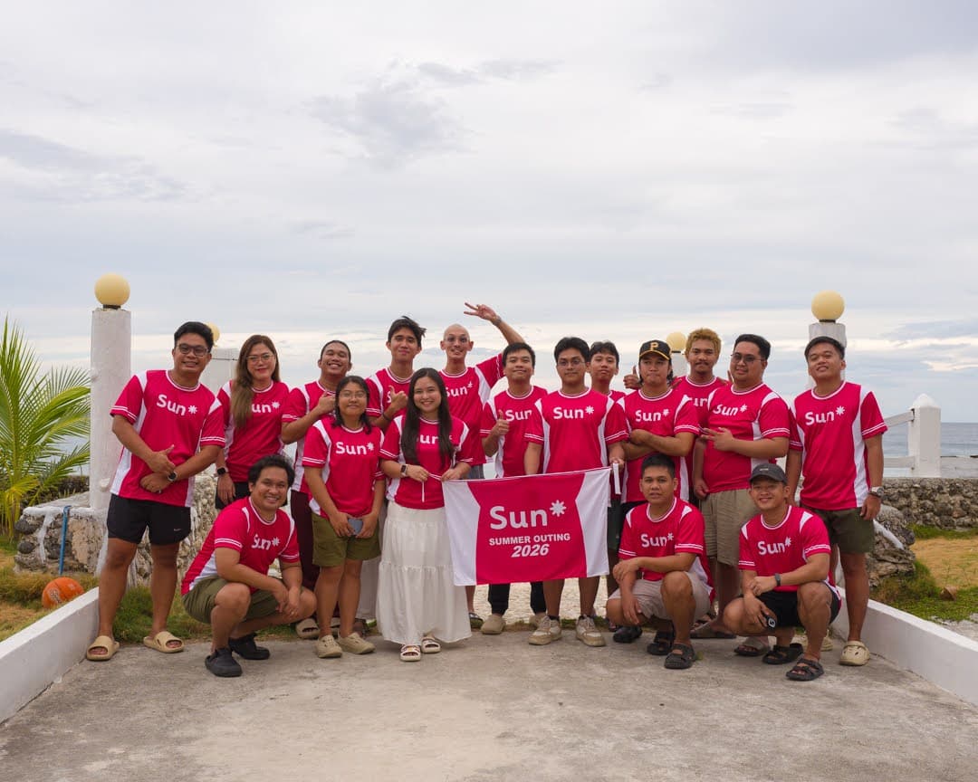 The team in matching Sun* shirts posing together at the beach.